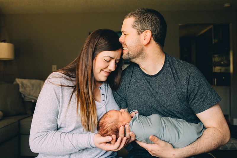 Fresh 48 Newborn Photography, a dad holds baby and leans into mom, they are both happy and taking in the moment