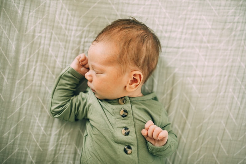 Fresh 48 Newborn Photography, a baby in a onesie lays sleeping on bed linens