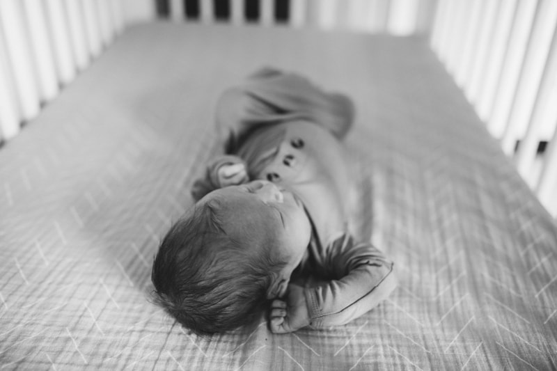 Fresh 48 Newborn Photography, a baby lays a crib sleeping in a onesie