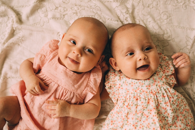Family Photography - two young smiling twin baby girls lay on a bed together