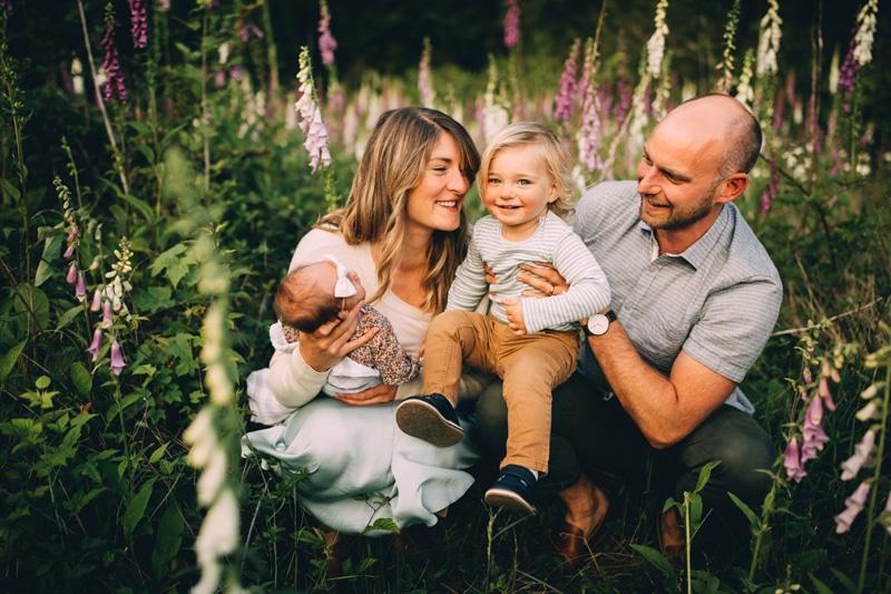 Family Photography - Mom and dad sit in a meadow of lavender as they admire their toddler while holding onto his newborn sister happily