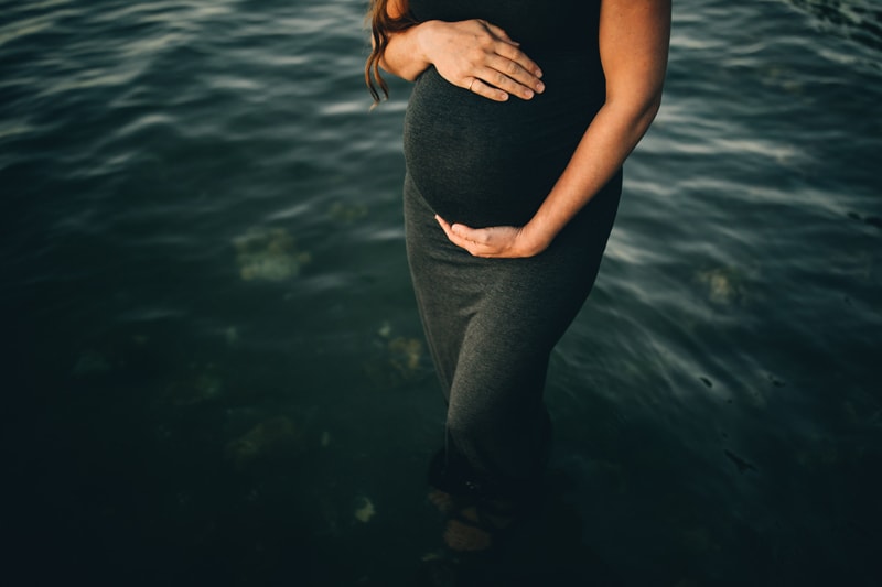 Family Photography - a pregnant woman stands in shallow water, she holds her belly