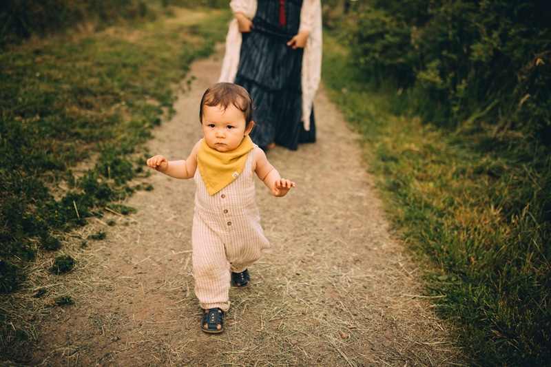 Family Photography - Little boy runs on trail through the grass, mom follows behind