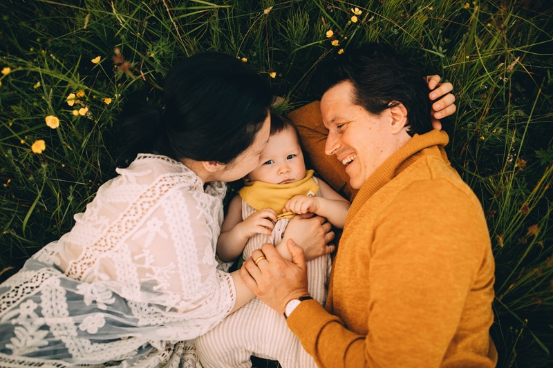 Family Photography -  a father and mother dote over their baby boy while laying in the grass