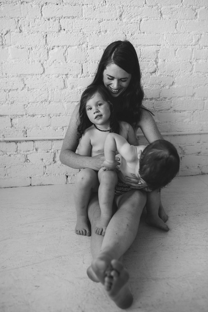Family Photographer, a little girl and boy sit close with mom at home all happy