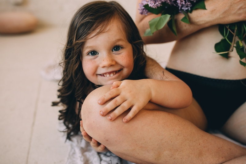 Motherhood Photography, a little girl leans on her mom's leg happy to be close