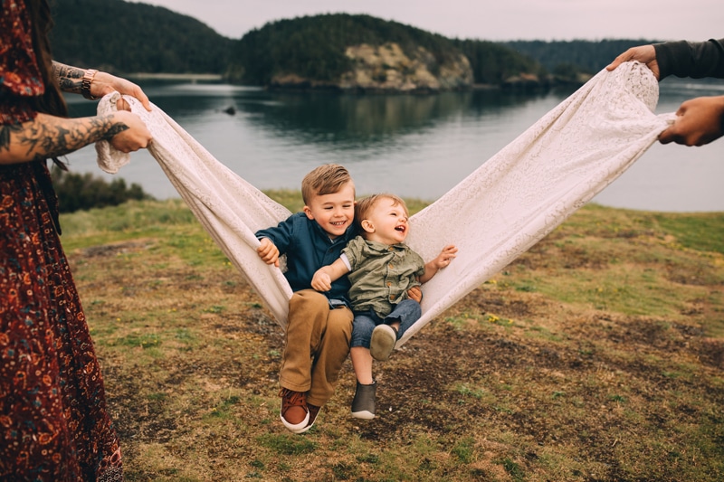 Family Photographers, two brother's swing in a blanket outdoors as their parents rock them playfully