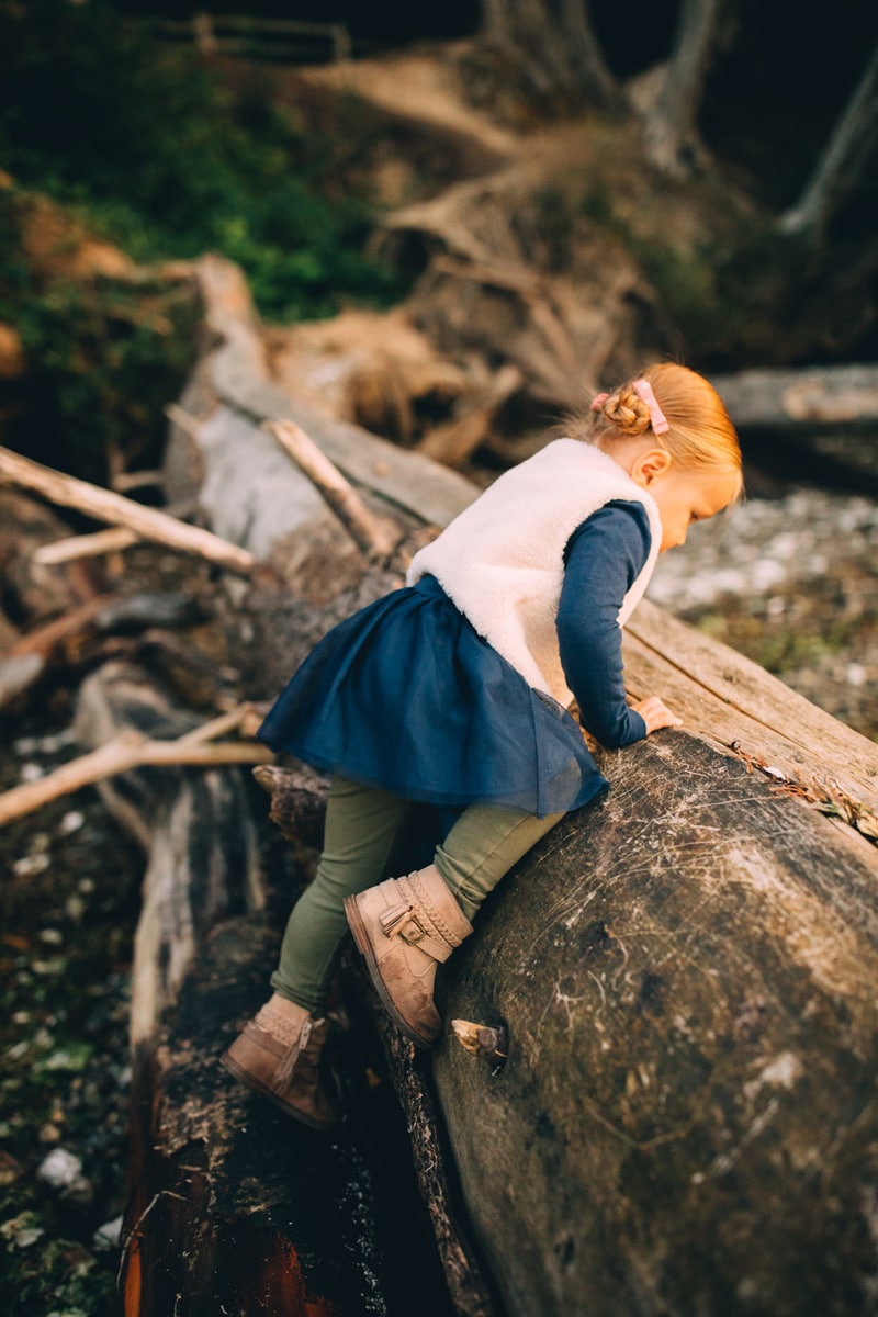 Milestone Photography, a little girl leans over a log curiously to explore