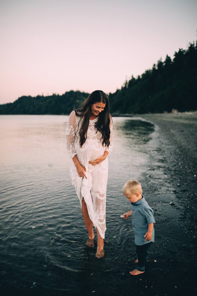 Family Photographer, a young pregnant expecting woman walks barefoot in the lake with her young son