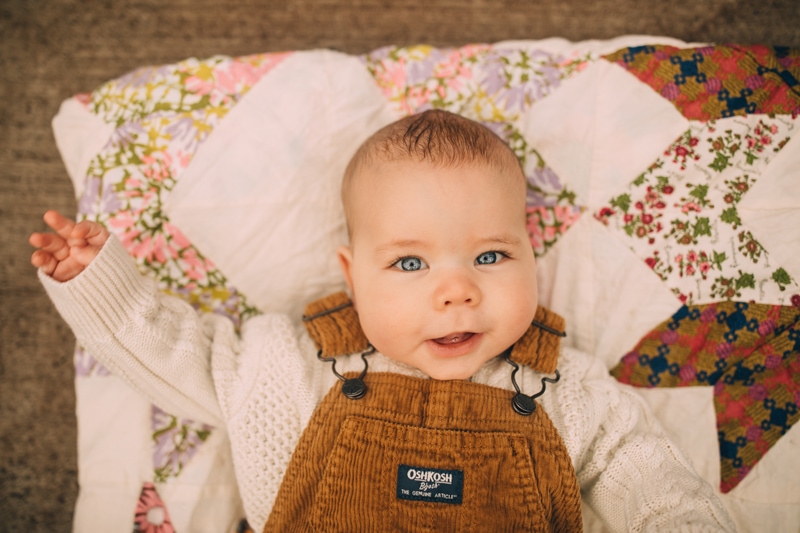 Milestone Photography, a baby lays on a floral quilt wearing OshKosh BGosh overalls