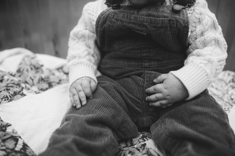 Milestone Photography, a little baby in corduroy overalls sits on a bed with floral covers