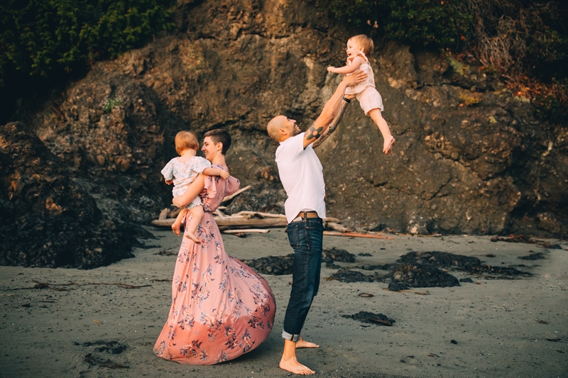 Family Photography, a father tosses baby girl into the air playfully as mom danced with their other baby girl on the beach