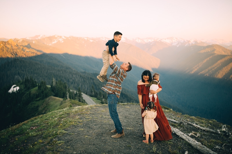 Family Photographer, Dad tosses son into the air as he laughs, mom and sisters are near by on the same hillside