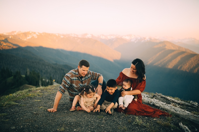 Family Photographer, a dad, mom, and three young children sit in the grass in the mountains