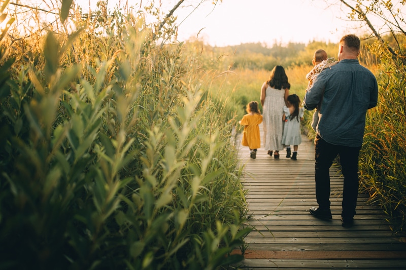 Family Photographer, A young mother crosses a small wooden plank pathway through reeds, Dad and daughters folllow her