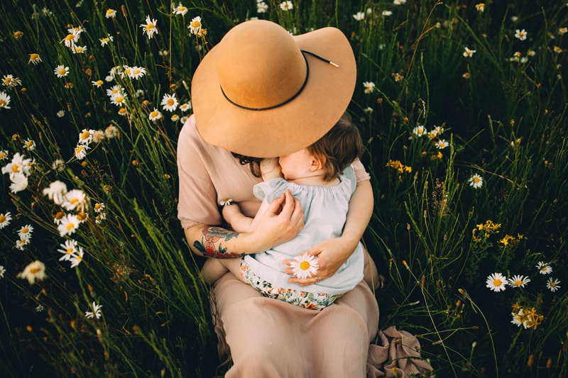 Motherhood Photography, a mother holds her baby girl as they sit in a bed of wildflowers