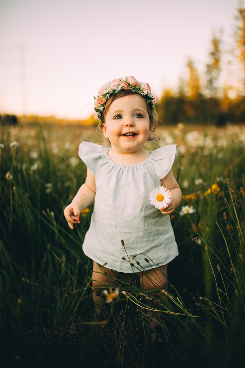 Motherhood Photography, a young baby girl holds a flower and wears a flower crown in a flower field