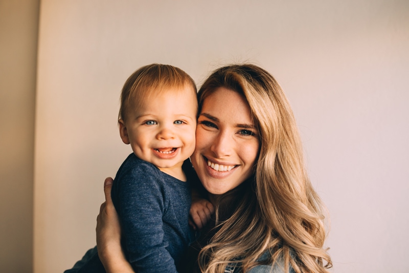 Motherhood photographer, a young mom holds baby at home, they both smile