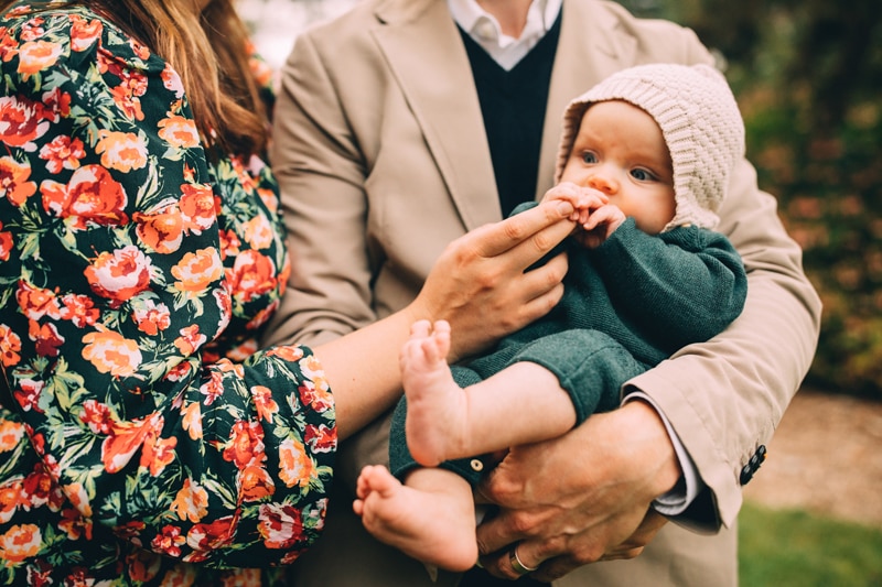 Family photographer, dad holds baby and mom let's baby hold onto her hands comforting him