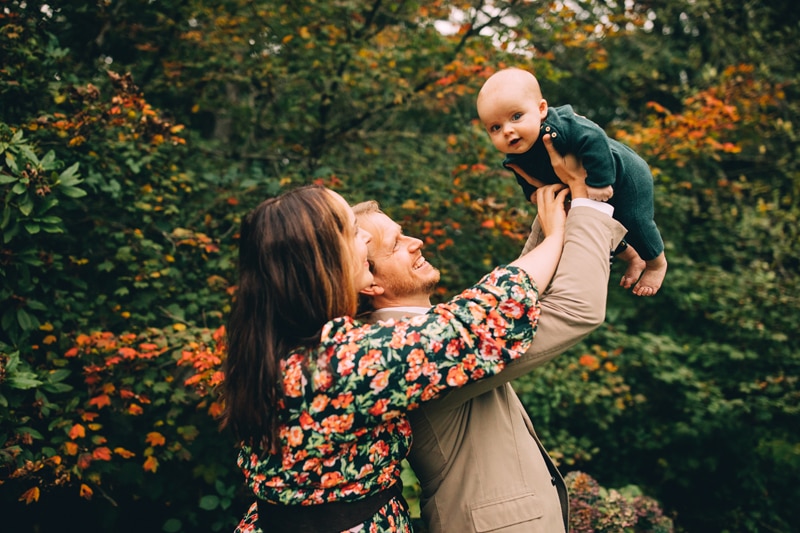 Family Photography, Mom and dad lift their happy baby into the air. They are all dressed up outside in the garden