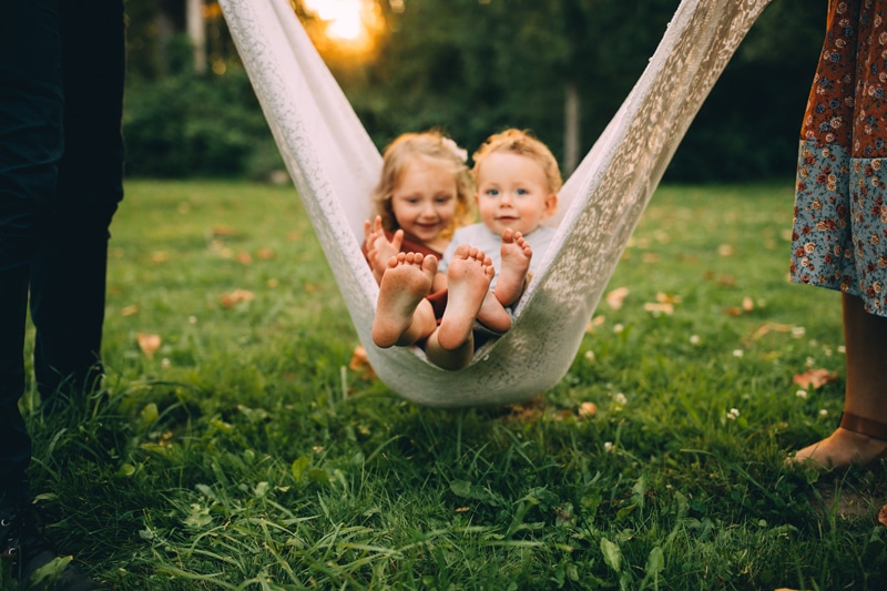 Family Photographer, a toddler boy and girl swing in the sheets as their parents rock them gently outside