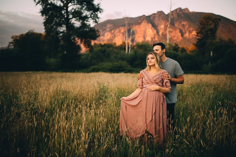 Family Photographer, a couple, man and woman, hold each other close outdoors in a grassy field