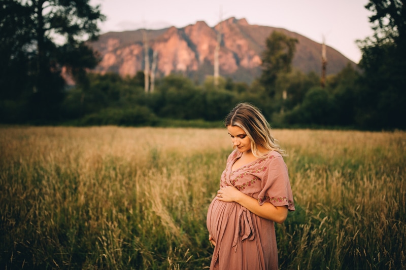 Family Photography, a pregnant woman holds her belly in a grassy meadow near the forest