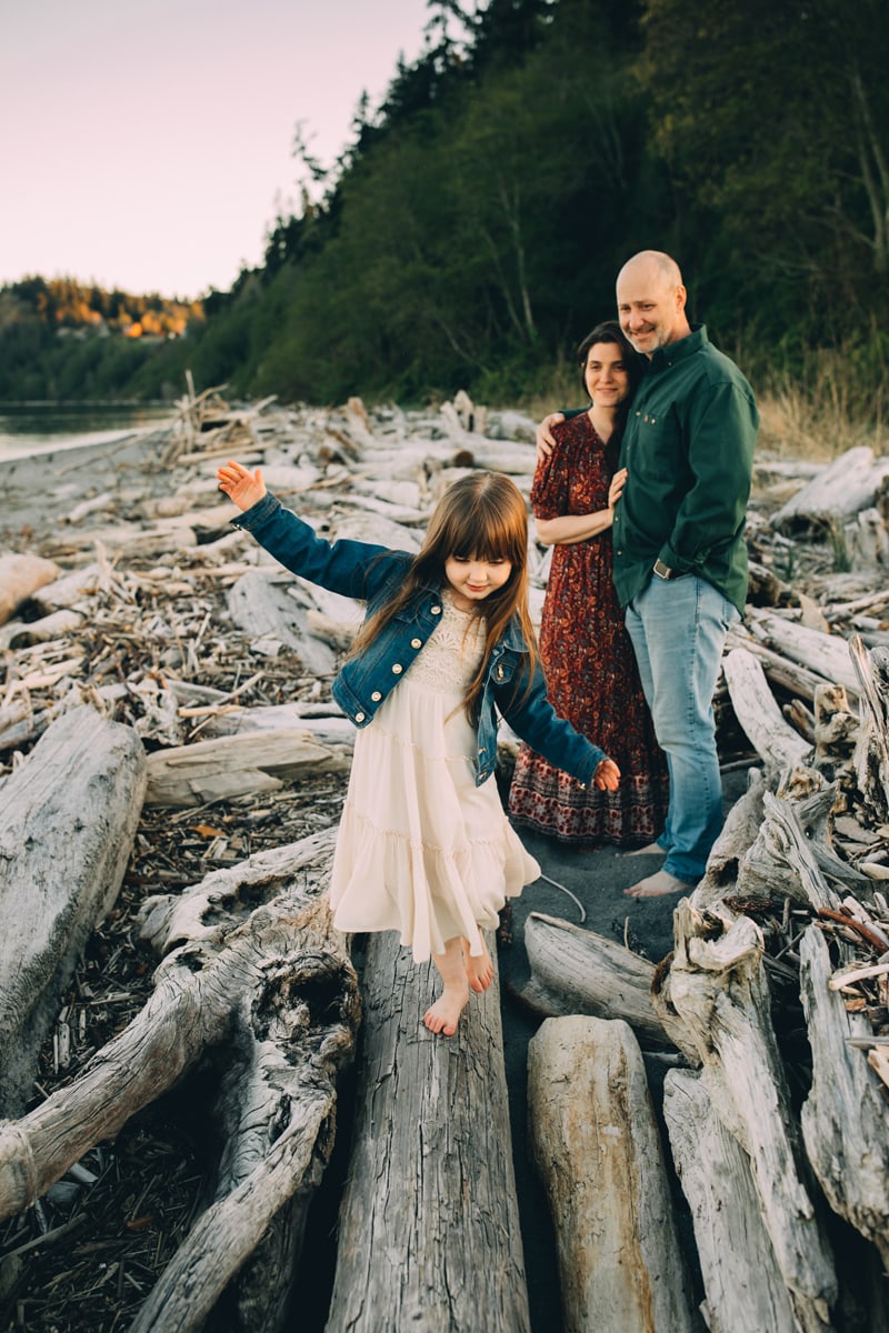 Family Photographer - Mom and dad watch their young daughter balance atop a dry log near the river.