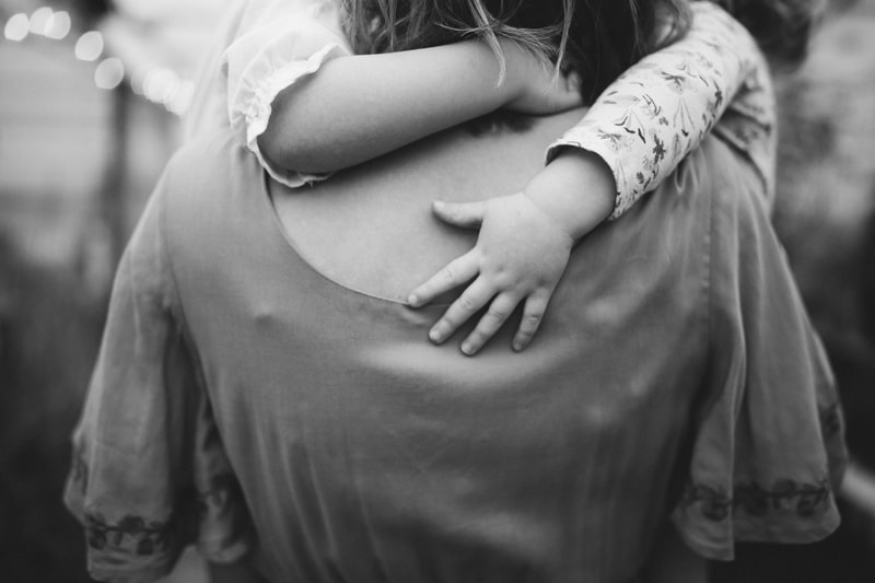 Motherhood Photography, a small girl wraps her arms around her mother as she is carried