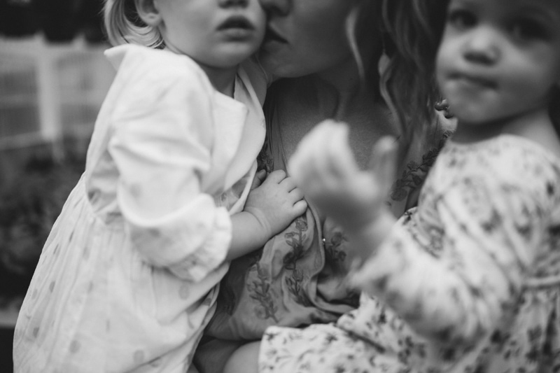 Motherhood photography, a mom kisses one of her daughters as she holds both of them in her arms