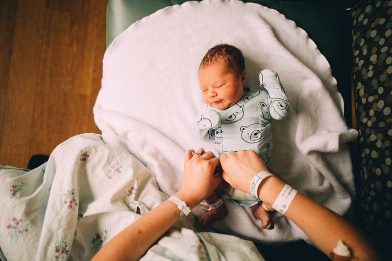Fresh 48 Newborn Photography, a baby is changed on a hospital couch by new mom, baby looks content