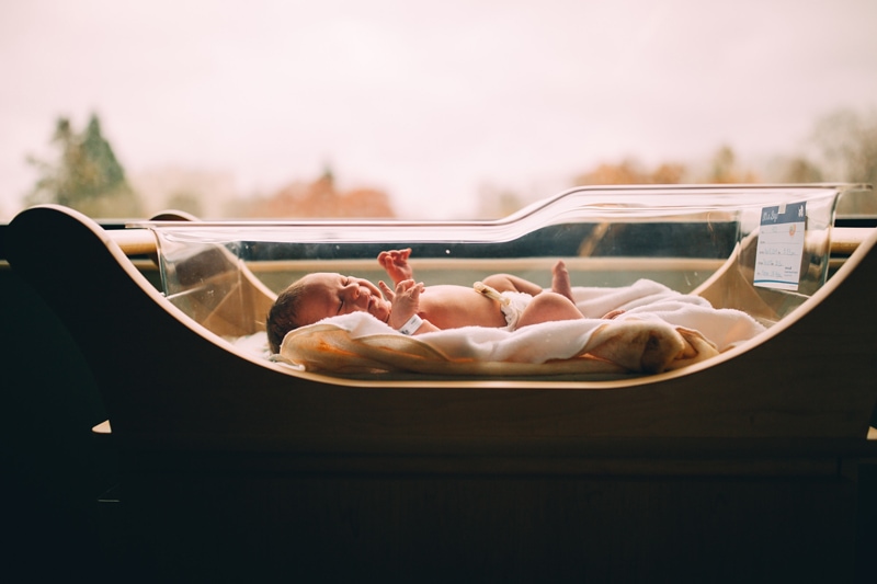 Fresh 48 Newborn Photography, a baby lays in a hospital bassinet near a window's light