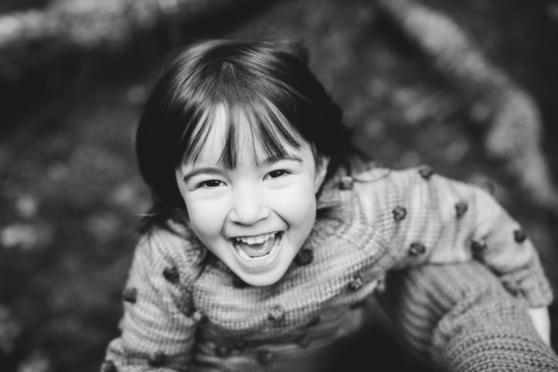 Motherhood photography - a little girl in a knit sweater smiles playfully outside