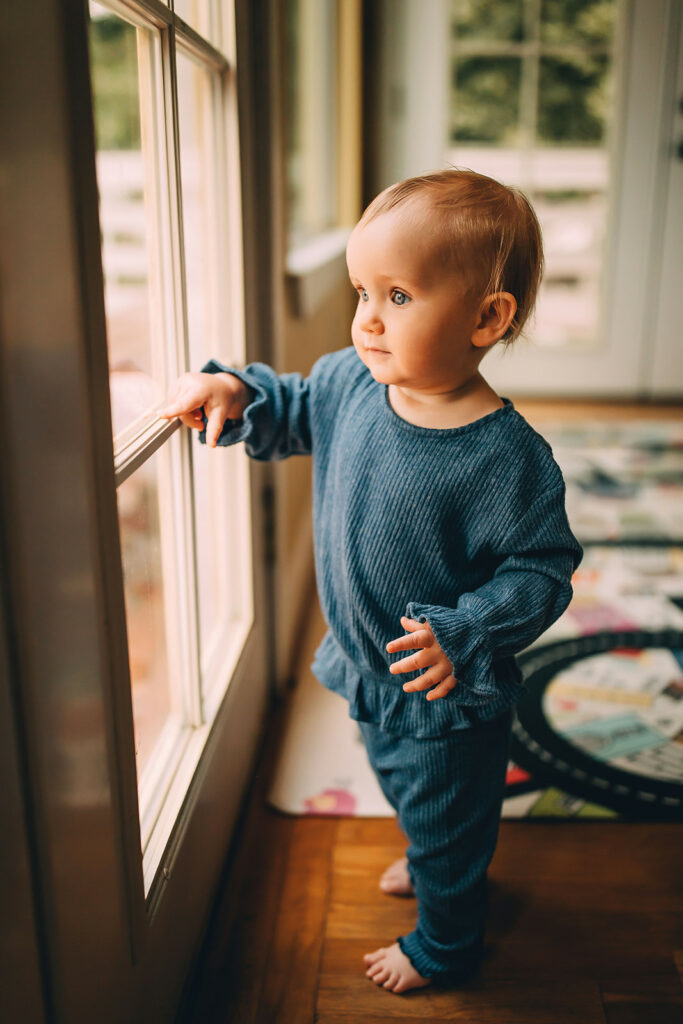 Baby standing and pointing out a window during motherhood session