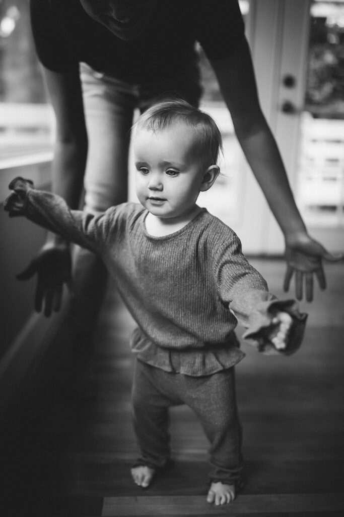 Mother helping baby walk during in home motherhood session